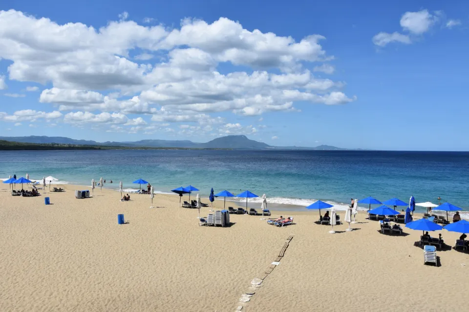 Sandstrand mit blauen Sonnenschirmen an der Bucht von Sosúa, im Hintergrund die Berge.